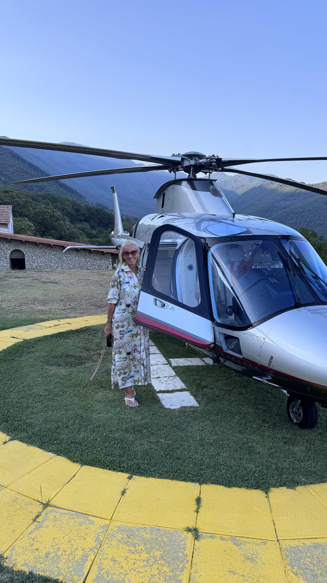 Susi beside a private helicopter on a hillside landing pad