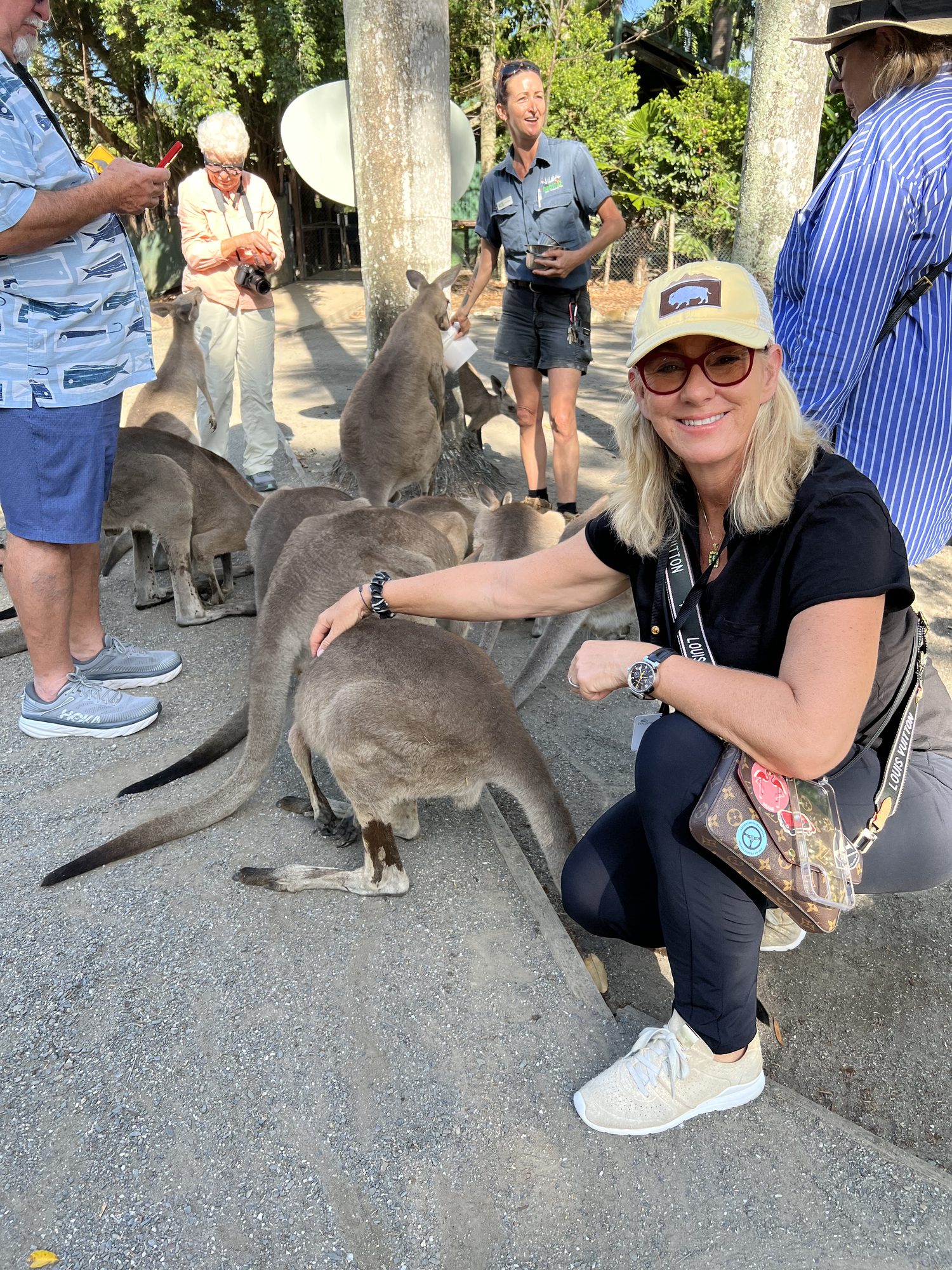 Susi kneeling to pet a kangaroo among a mob of grey kangaroos