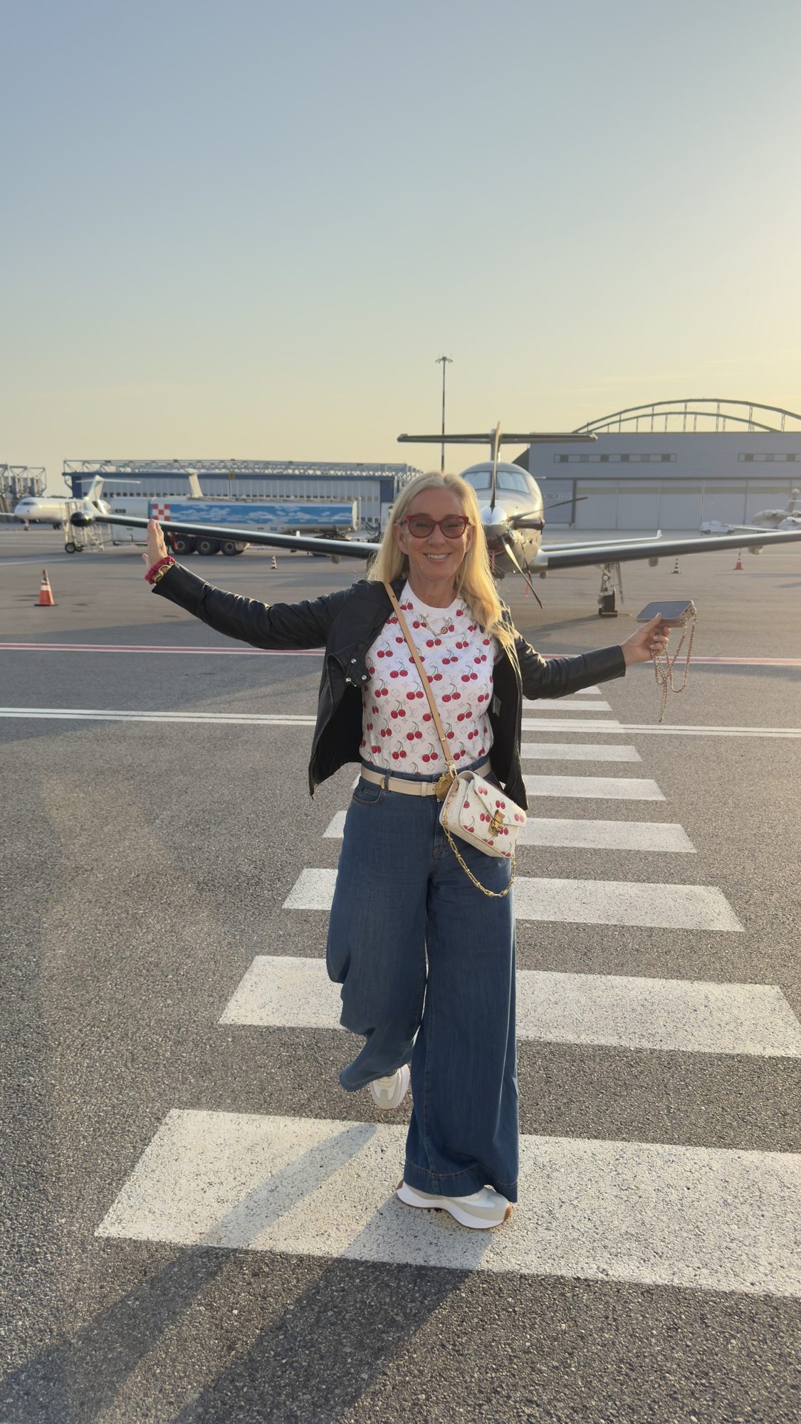 Susi with arms wide on the tarmac, private jets behind her at golden hour